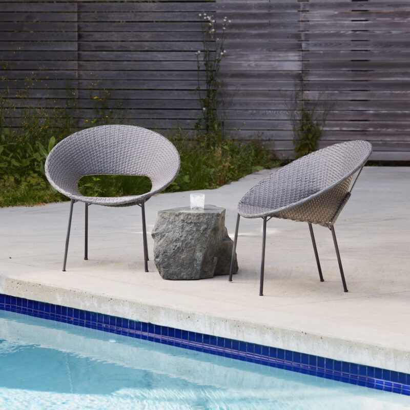 The Ebb boulder is surrounded by two patio chairs beside a pool.