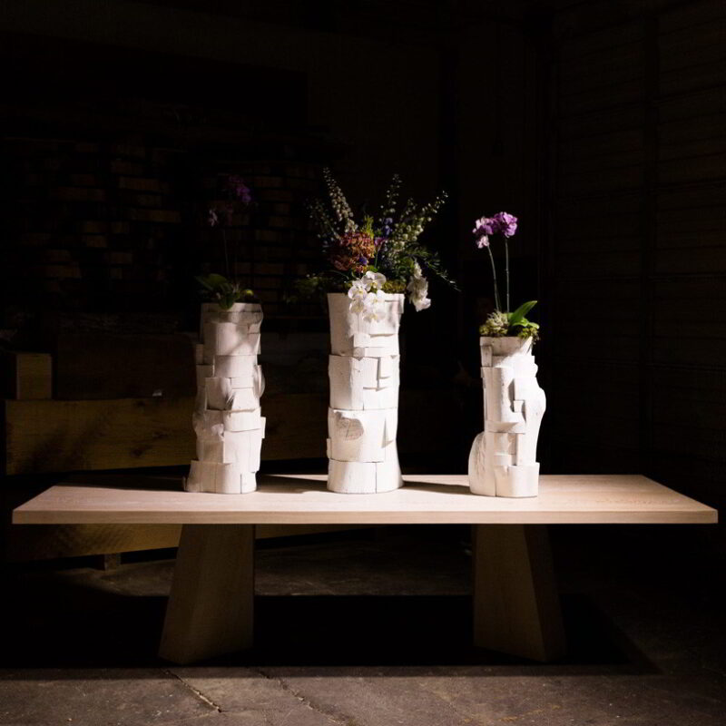 Three flower-filled vessels on a Soma Dining table.