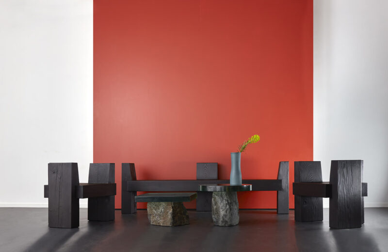 The beton brut bench chairs are pictured against a red background. they are surrounding two flow side tables.