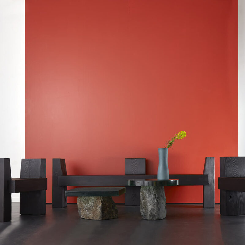 The beton brut bench chairs are pictured against a red background. they are surrounding two flow side tables.